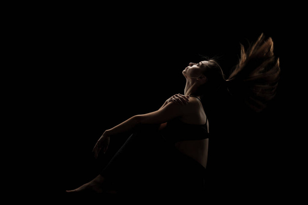 cute caucasian girl sitting with her hair in the air against dark backgroung. side lit silhouette. - Foto, immagini