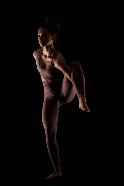 Fit woman practicing yoga poses. Side lit half silhouette girl doing exercise in studio against black background. - Foto, Imagem