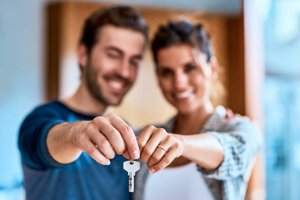 We finally got the place we always wanted. Portrait of a cheerful young couple holding a key together to their new home while standing inside during the day. - Φωτογραφία, εικόνα