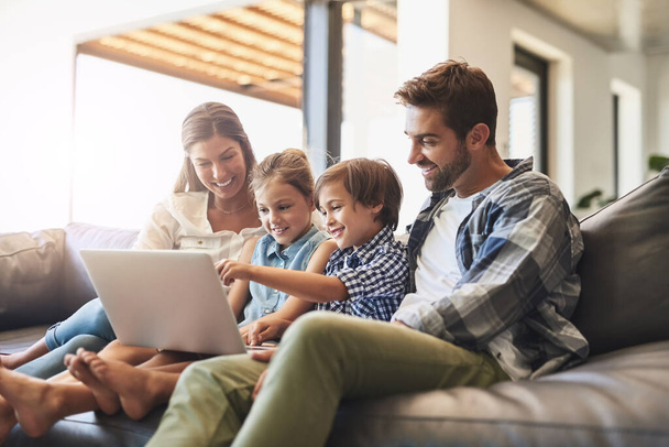 Online és mint egy család. Egy anyáról és apáról, akik laptopot használnak a fiukkal és a lányukkal otthon a kanapén.. - Fotó, kép