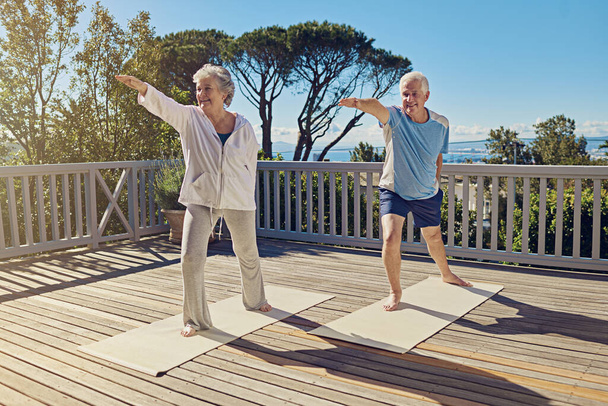 They love getting their yoga on. Shot of a senior couple doing yoga together on their patio outside. - Φωτογραφία, εικόνα