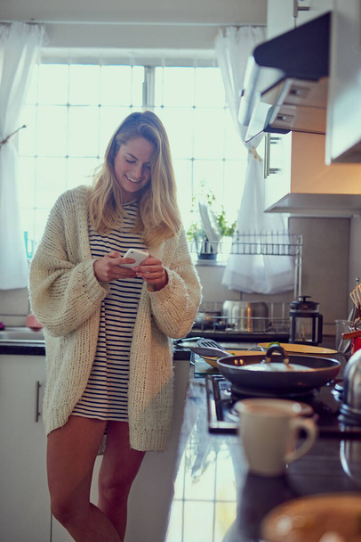 Lunch is ready, where are you. Cropped shot of an attractive young woman texting on a cellphone while cooking in her kitchen. - Photo, Image
