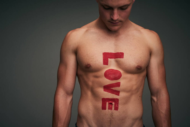Liebe dich selbst. Studioaufnahme eines jungen Mannes ohne Hemd vor grauem Hintergrund mit dem Wort Liebe auf der Brust. - Foto, Bild
