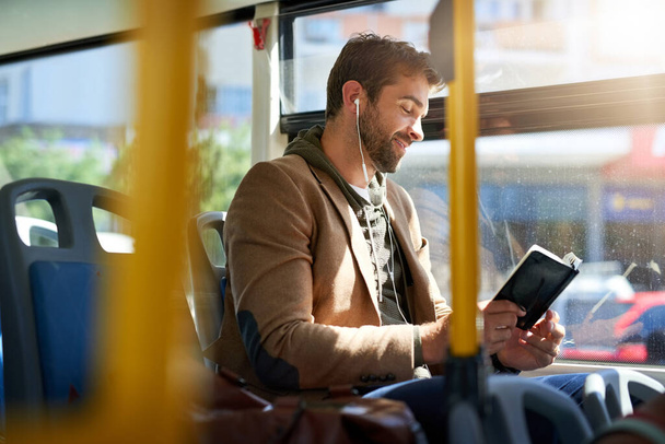 Checking out the best tourist spots. Cropped shot of a handsome young man reading a book during his morning bus commute. - Zdjęcie, obraz