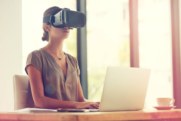Fare affari oltre i confini. Girato di una giovane donna d'affari che indossa un visore VR mentre lavora in un ufficio. - Foto, immagini