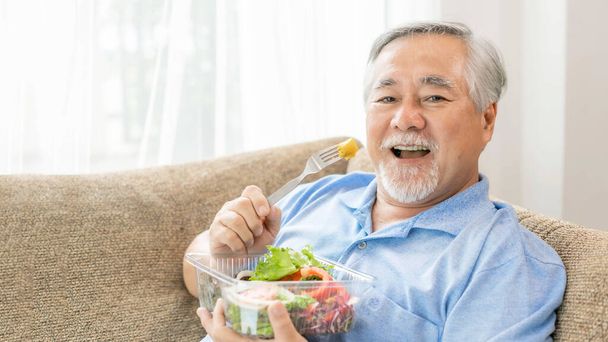 Lifestyle senior man feel happy enjoy eating diet food fresh salad on sofa - Фото, зображення