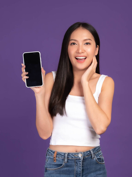 Beautiful Asian brunette woman cute girl in white tank top ,Excited surprised girl showing smart phone with blank screen , black screen isolated purple background , Mock Up Image - Foto, imagen