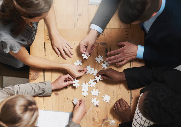 Putting their vision together. High angle shot of a group of businesspeople building a puzzle together in an office. - Foto, afbeelding