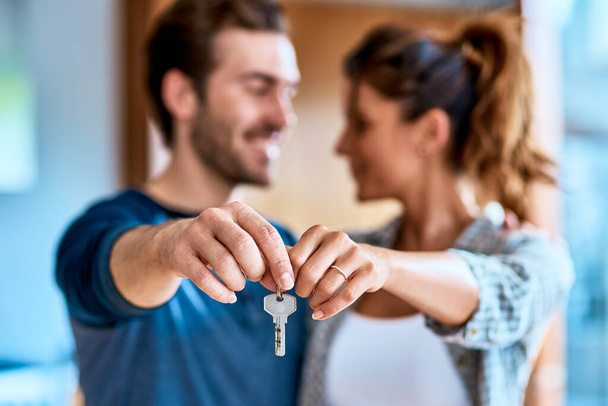 Die Schlüssel zu unserem neuen Zuhause. Aufnahme eines fröhlichen jungen Paares, das tagsüber einen Schlüssel für sein neues Zuhause zusammenhält, während es drinnen steht. - Foto, Bild