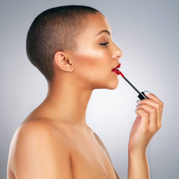 I like my lips bold. Studio shot of a beautiful young woman applying red lipstick against a grey background. - Фото, изображение