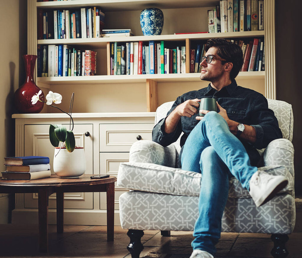 Surgen nuevas posibilidades cada nuevo día. Tiro de un joven hombre de negocios guapo bebiendo café mientras está sentado en un sofá en su oficina en casa. - Foto, imagen