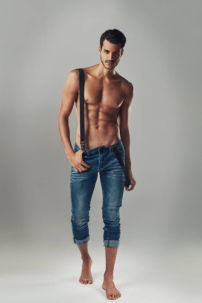Набирання статі. Студійний знімок красивого молодого чоловіка в джинсах і підтяжках на сірому фоні
. - Фото, зображення