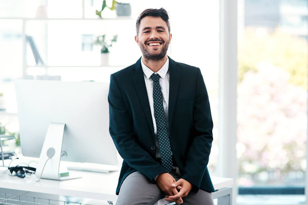 Id like to think the white collar life chose me. Cropped portrait of a handsome young businessman smiling while sitting on his desk in a modern office. - Foto, Imagen