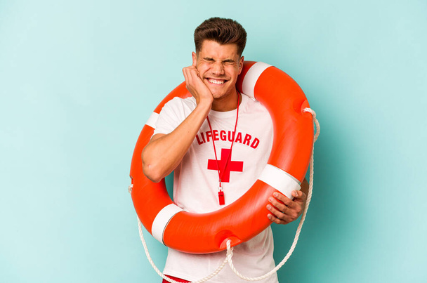 Young caucasian lifeguard isolated on blue background covering ears with hands. - Photo, Image