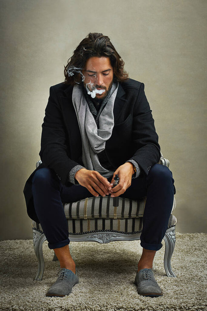 Taking a moment for himself. Shot of a stylishly dressed man smoking an electronic cigarette while sitting in the studio. - Foto, Imagen