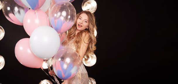 attractive young woman in a dress with balloons black background, looking at the camera, emotions of surprise and delight. holiday or birthday concept. Banner. place for text - Photo, Image