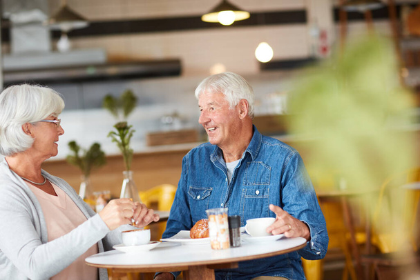 カッパに追いつくために。コーヒーショップでコーヒーを飲みながらリラックスした幸せな高齢者のカップルのショット. - 写真・画像