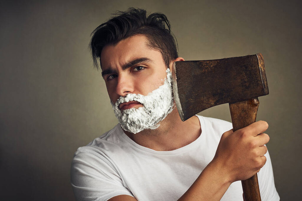 Its the right tool for the job. Shot of a handsome young man shaving his beard with a lumberjack. - Foto, Imagem
