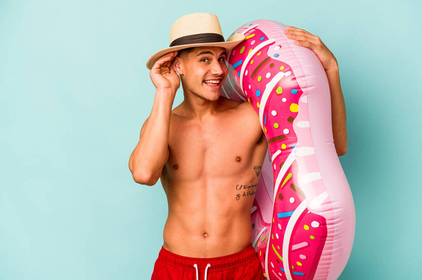 Young caucasian man holding an inflatable donut isolated on blue background trying to listening a gossip. - Valokuva, kuva
