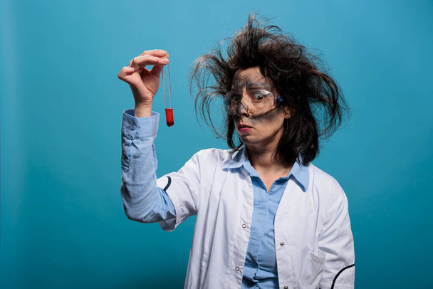 Insane anxious looking scientist analyzing chemistry glass tube filled with blood sample. - Foto, imagen