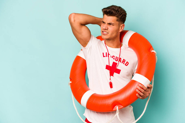Young caucasian lifeguard isolated on blue background touching back of head, thinking and making a choice. - Fotografie, Obrázek