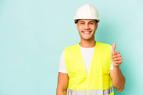 Young laborer caucasian man isolated on blue background smiling and raising thumb up - Foto, Imagem