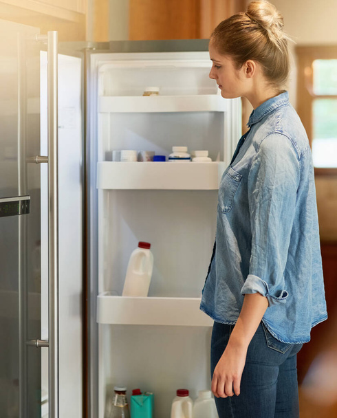 When hunger strikes.... Cropped shot of a young woman looking inside her fridge at home. - 写真・画像