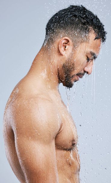 The shower is the best place to get lose in your thoughts. Studio shot of a handsome young man taking a shower against a grey background. - Foto, imagen