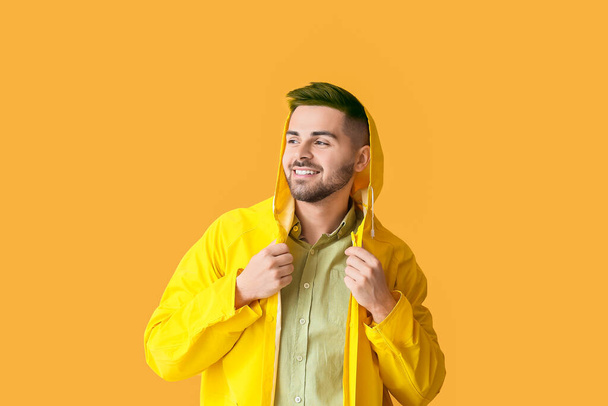 Stijlvolle jongeman met ongewoon haar in regenjas op oranje achtergrond - Foto, afbeelding