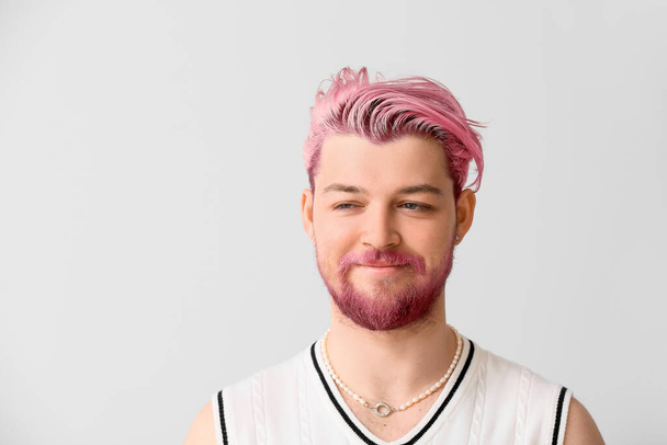 Стильный улыбающийся молодой человек с необычными розовыми волосами и бородой на светлом фоне - Фото, изображение