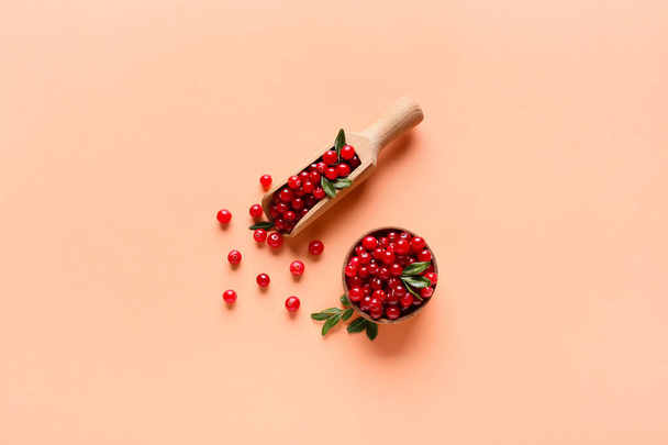 Wooden spoon and bowl with lingonberries on beige background - Photo, image