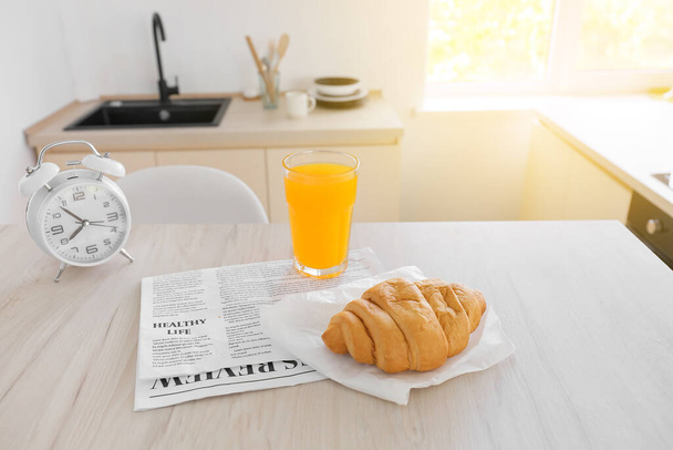 Tasty croissant, glass of juice and newspaper on dining table in kitchen - Foto, imagen