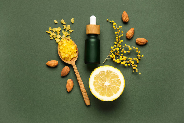 Bottle of natural serum, spoon with sea salt, almond nuts, lemon and flowers on green background - Fotografie, Obrázek