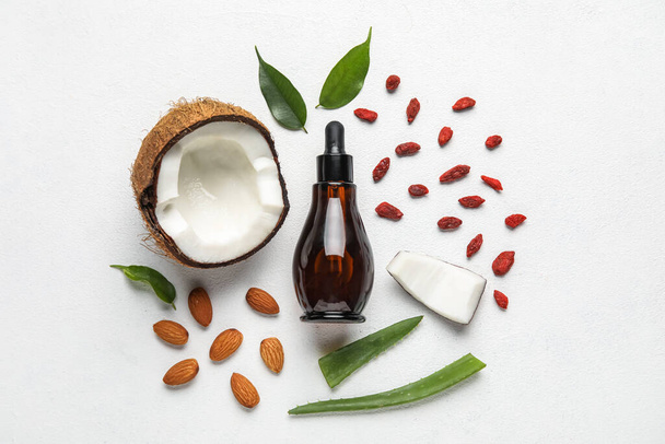 Bottle of natural serum with coconut, plant leaves, goji berries and almond nuts on white background - Valokuva, kuva