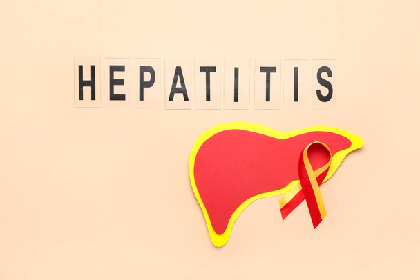 Awareness ribbon with word HEPATITIS and paper liver on beige background - Фото, изображение