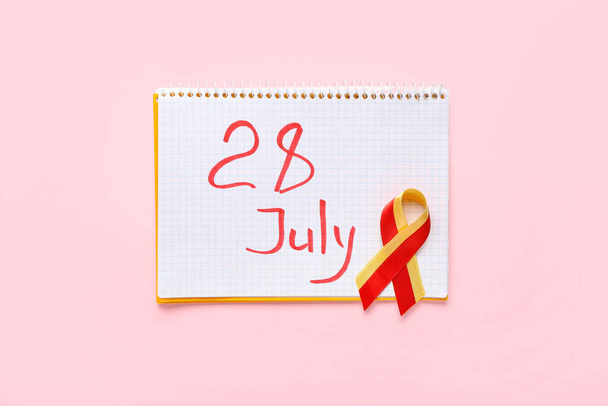 Bewusstseinsband und Notizbuch mit Datum 28. Juli auf rosa Hintergrund. Welt-Hepatitis-Tag - Foto, Bild