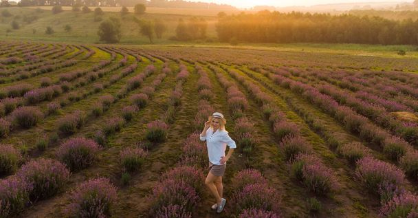drone videó ingyenes és boldog fiatal nő fut rózsaszín és lila levendula mezők naplementekor - Fotó, kép