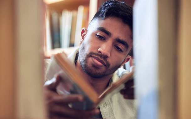 Čím víc stránek otočíte, tím víc se naučíte. Snímek mladého muže, který si vybírá knihu ke čtení z knihovny na vysoké.. - Fotografie, Obrázek