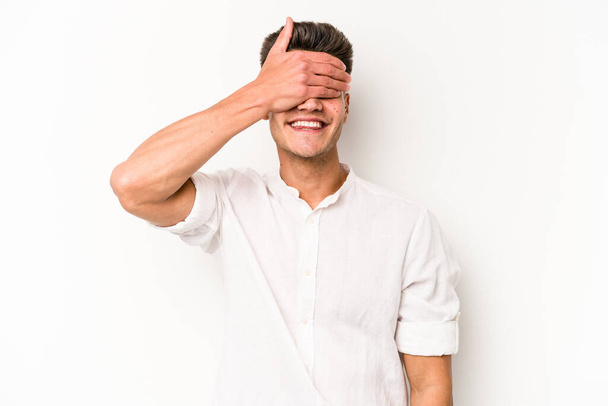 Молодий кавказький чоловік ізольований на білому тлі покриває очі руками, посміхається широко чекаючи сюрпризу
. - Фото, зображення