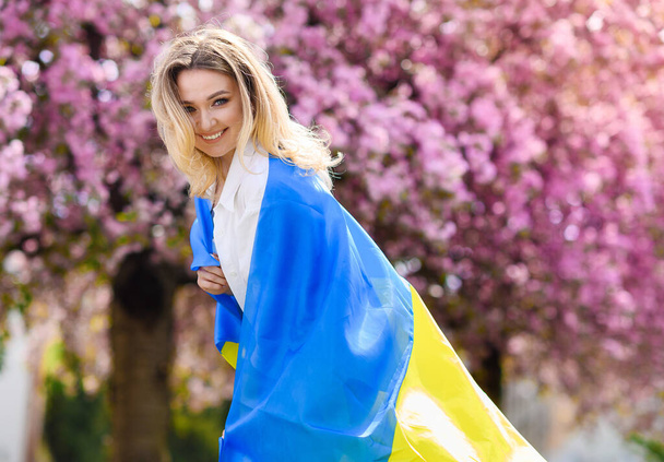 Гарна блондинка у білій сорочці тримає прапор України.  - Фото, зображення