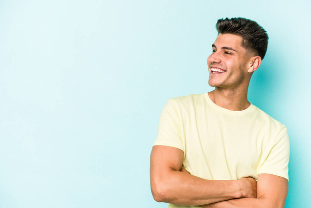 Young caucasian man isolated on blue background smiling confident with crossed arms. - Photo, Image