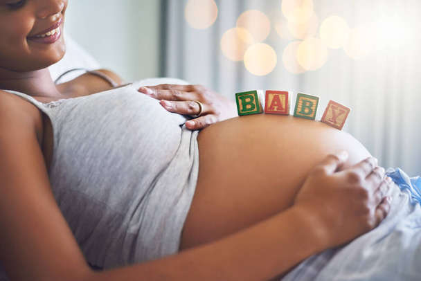 Ik ben zo klaar om moeder te worden. Gehakt schot van een zwangere vrouw met houten blokken op haar buik die het woord baby spellen. - Foto, afbeelding