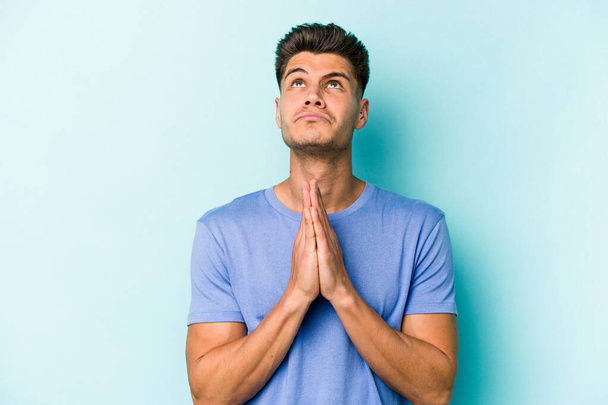 Mladý běloch izolovaný na modrém pozadí drží ruce v modlitbě blízko úst, cítí se sebejistý. - Fotografie, Obrázek