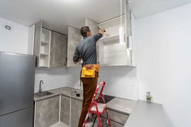 Kaukasischer Reparaturmeister Elektriker steht in Wohnung auf Leiter - Foto, Bild