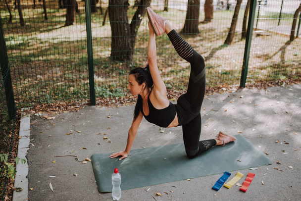 Young girl in black sportswear stretching and doing sport in park. Charming slim girl making aerobics. Concept of healthy lifestyle and training  outdoor in park. - Foto, afbeelding
