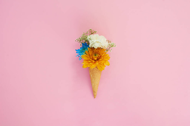 Anything looks good on a ice cream cone. Shot of a cone stuffed with flowers against a colorful background. - Foto, Imagen