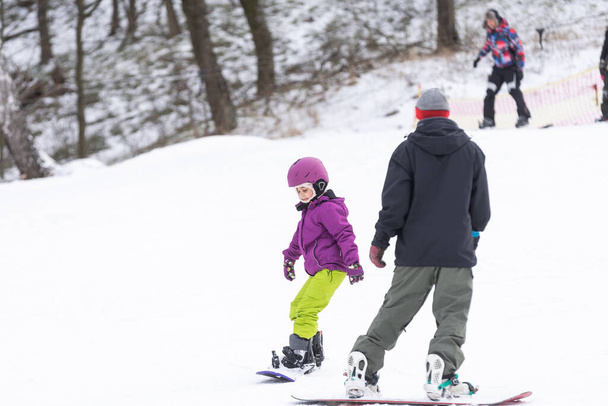 mała słodka dziewczyna uczy się jeździć na snowboardzie dla dzieci, sporty zimowe dla dziecka, bezpieczeństwo aktywnych sportów. - Zdjęcie, obraz