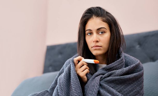 Het is officieel, ik heb griep. Schot van een jonge vrouw die haar temperatuur neemt terwijl ze herstelt van een ziekte in bed thuis.. - Foto, afbeelding
