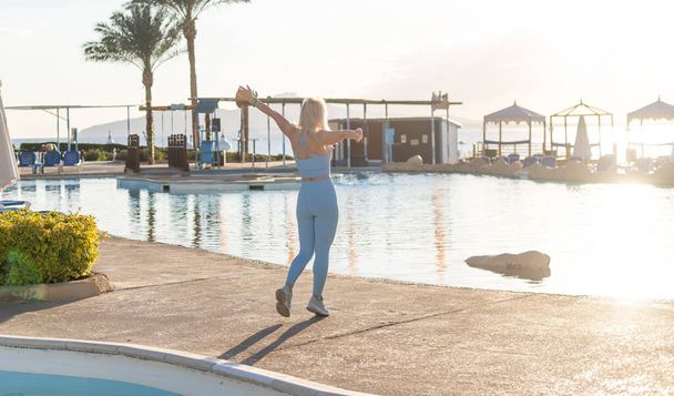 Доброе утро, йога медитирует на фоне восхода солнца. Активная женщина практикуется на вилле у бассейна, чтобы поддерживать форму и здоровье. Фитнес-тренировки для женщин, спортивные мероприятия на летний семейный отдых. - Фото, изображение