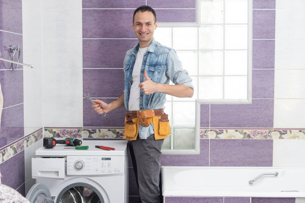 homem trabalhador encanador repara uma máquina de lavar roupa na lavanderia - Foto, Imagem